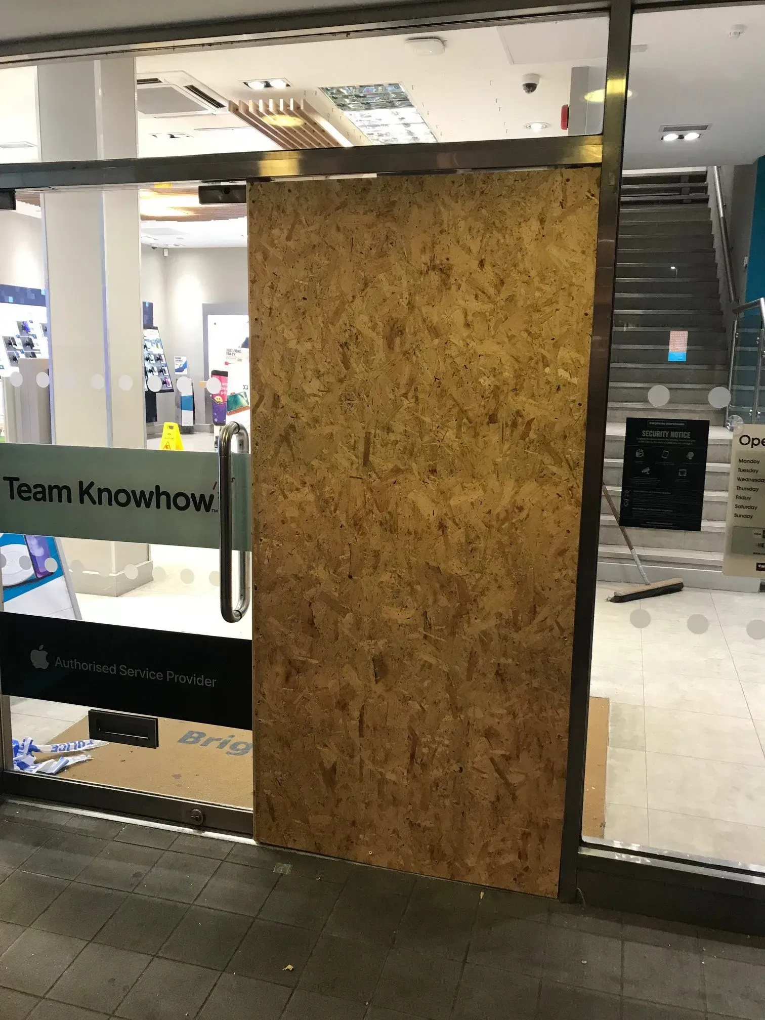 Boarded-up shop entrance; a large wooden panel covers a glass door. 