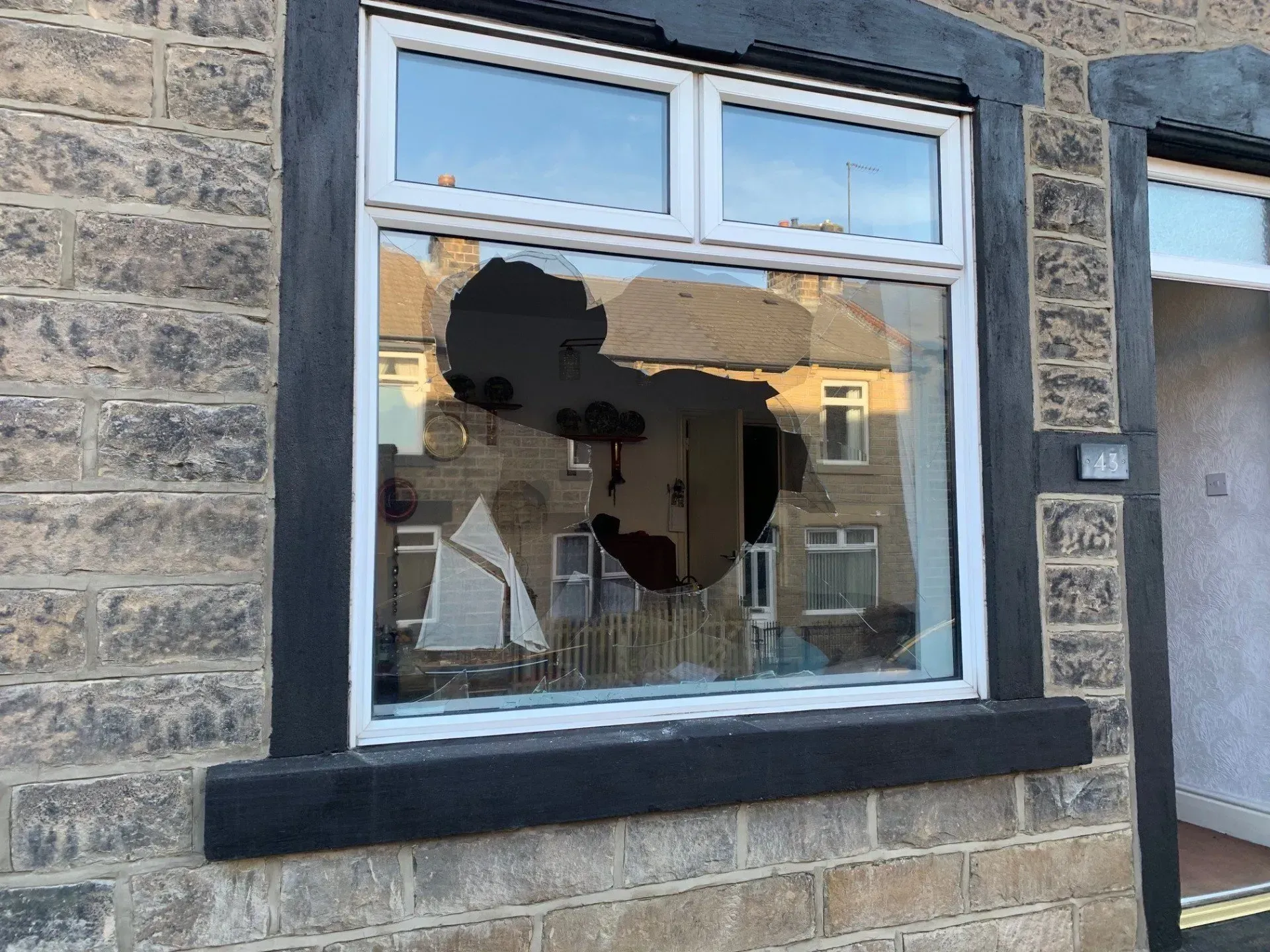 A window with a large hole in the glass, set in a stone house exterior.