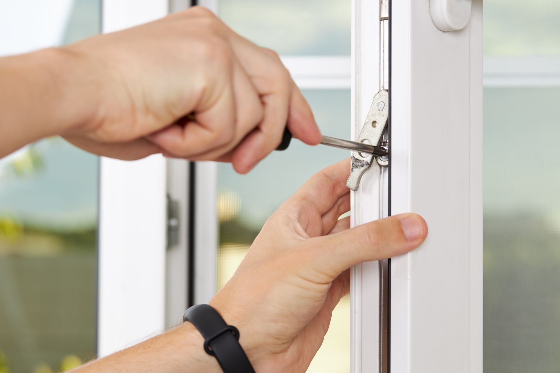 Hands using screwdriver to adjust window latch on white window frame.