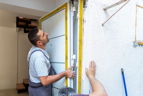 Two people installing a white door frame on a white stucco wall.