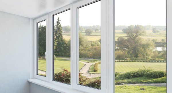 White-framed windows overlooking a green landscape with trees, fields, and a pathway.