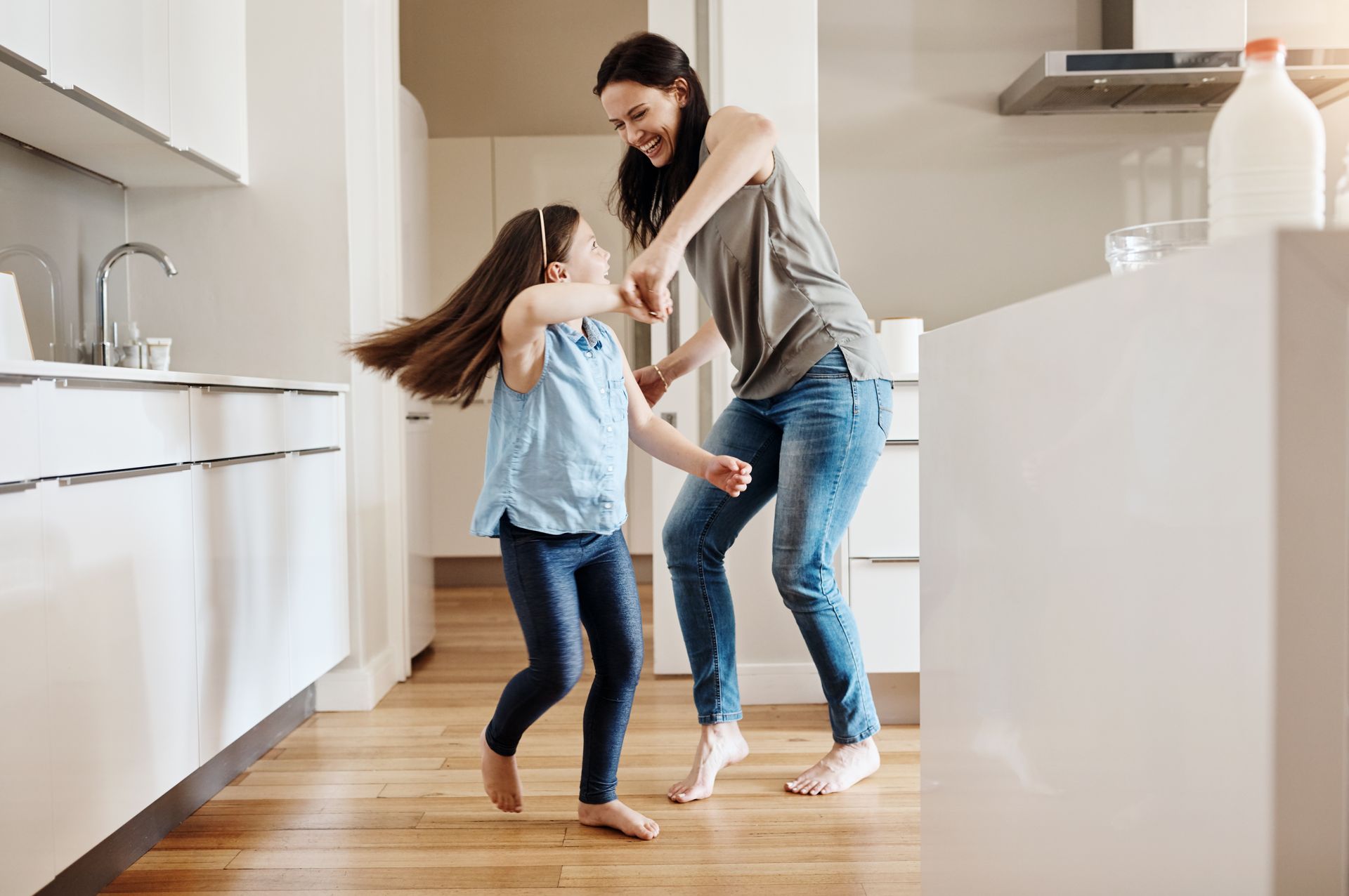 Woman and girl dancing joyfully in a modern kitchen.