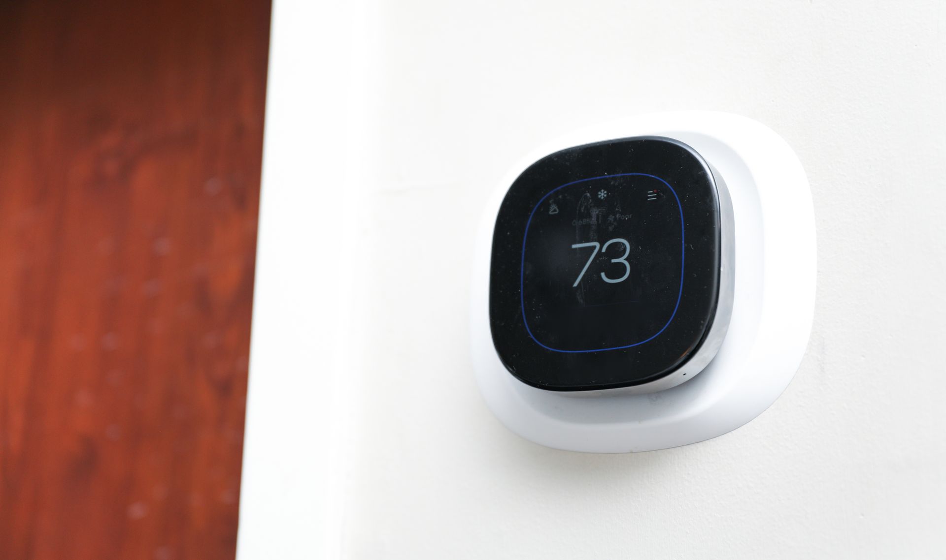 A smart thermostat displaying 73 degrees Fahrenheit on a white wall.