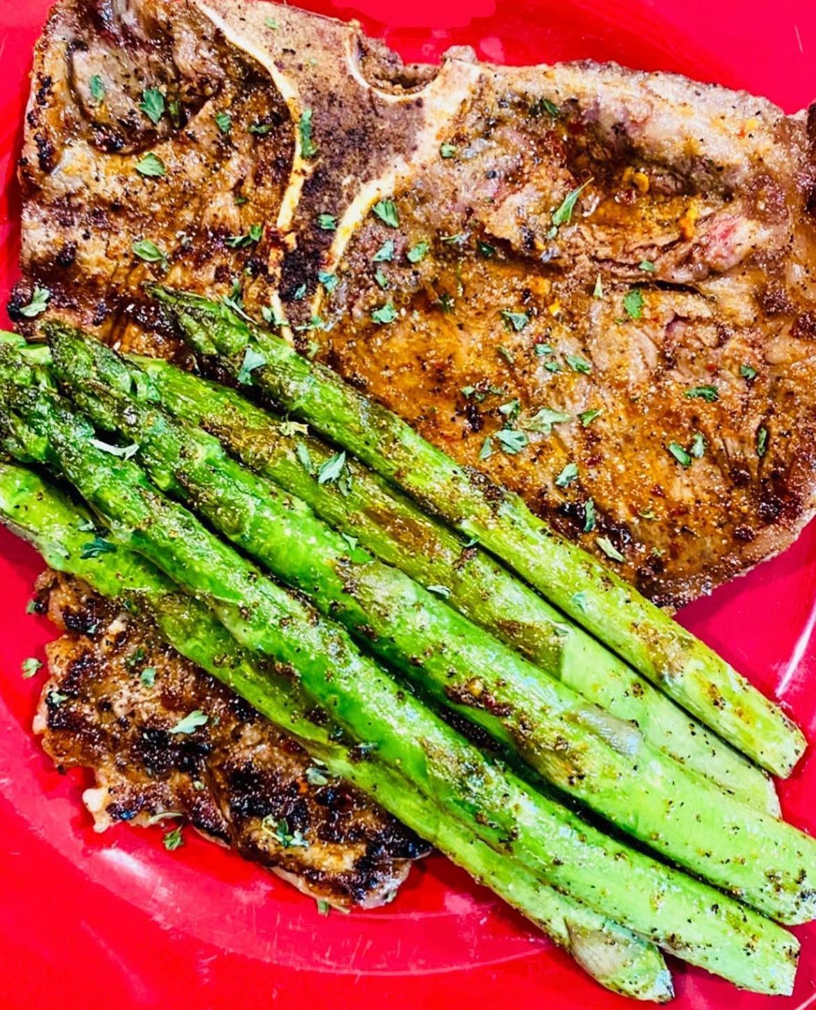 Grilled steak with seasoned asparagus on a red plate