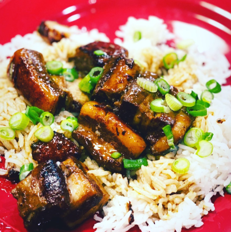 Rice bowl with glazed grilled meat and chopped green onions in a red bowl