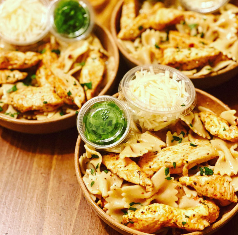 Bowls of pasta with grilled chicken, grated cheese, and green sauce on a wooden table