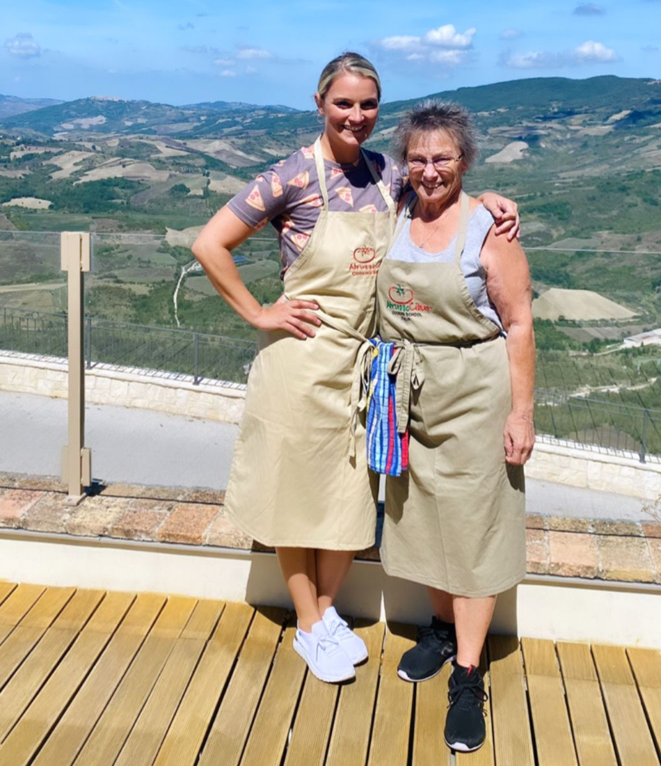 Chef partners in culinary aprons on an Italian hillside vineyard terrace