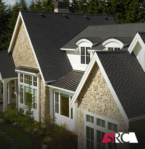 Stone and white house with black shingle roof and dormer windows.