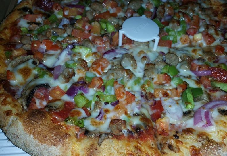 A pizza with lots of toppings and a pizza stand on top of it