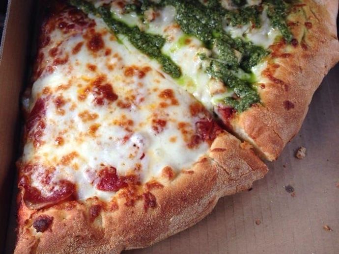 A slice of pizza with pesto on it is in a box.