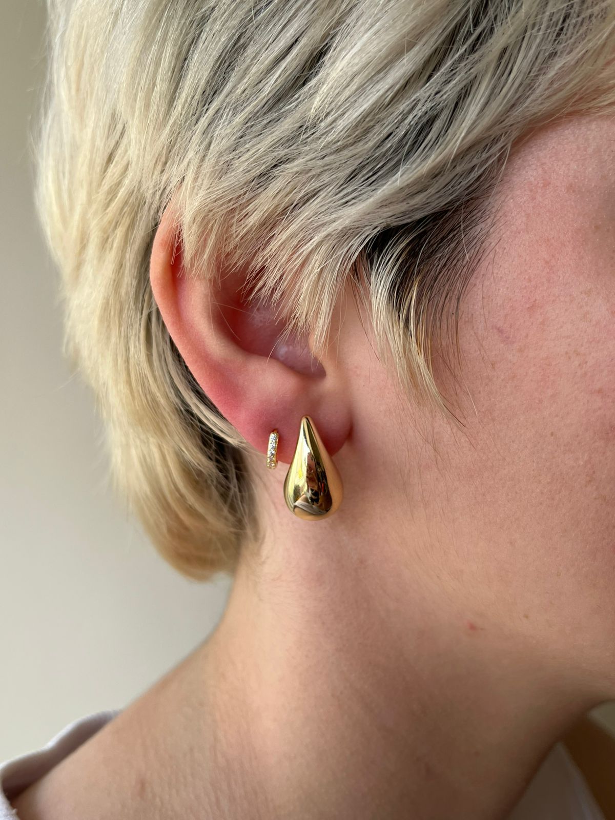 Primer plano de la oreja de una persona con cabello rubio corto y dos pendientes dorados en forma de lágrima.