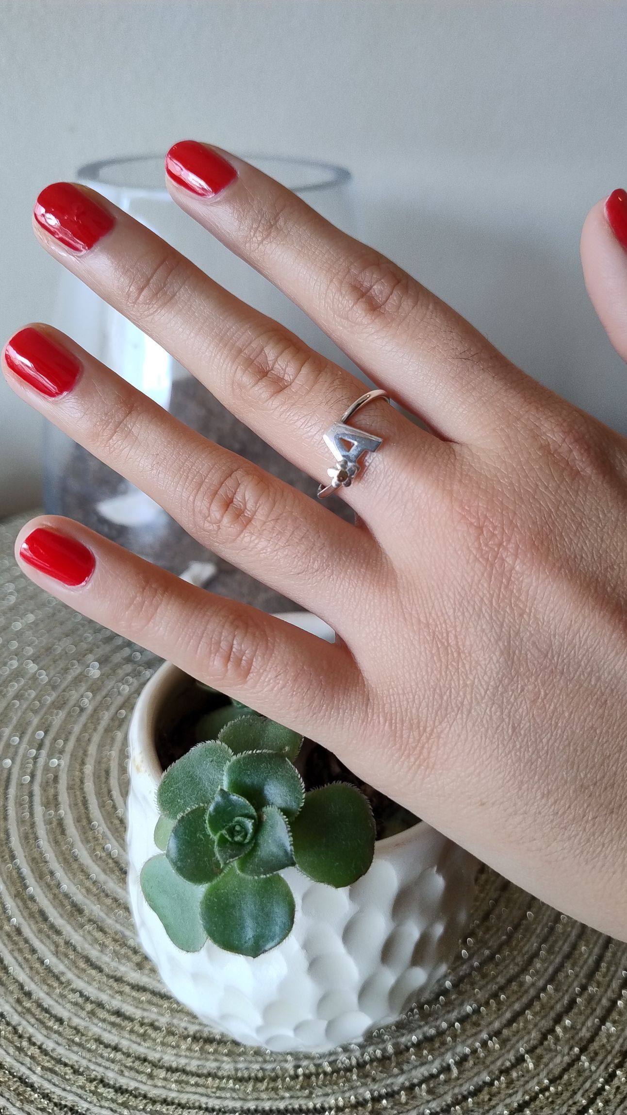Mano con esmalte de uñas rojo y un anillo de plata, descansando cerca de una pequeña planta suculenta.