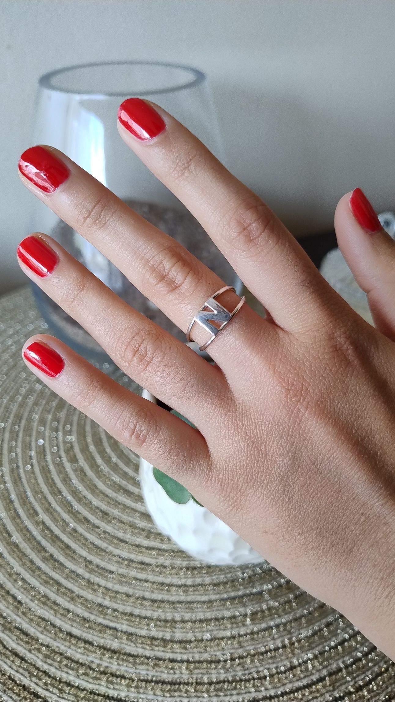Mano con uñas pintadas de rojo, luciendo un anillo de plata, descansando sobre una superficie de oro tejida.