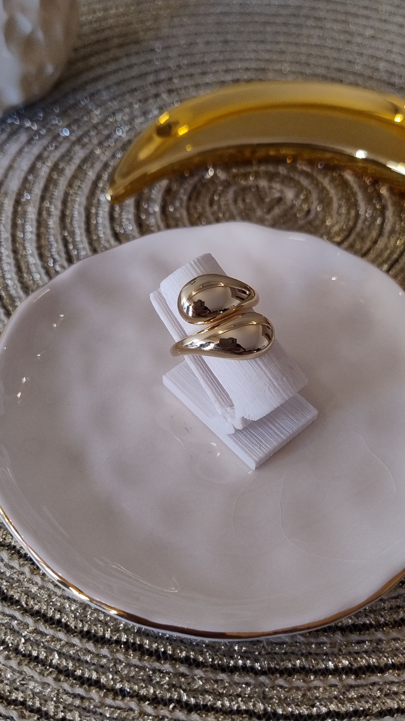 Mano con un anillo de oro de diseño estilizado, apoyada sobre una almohada morada.
