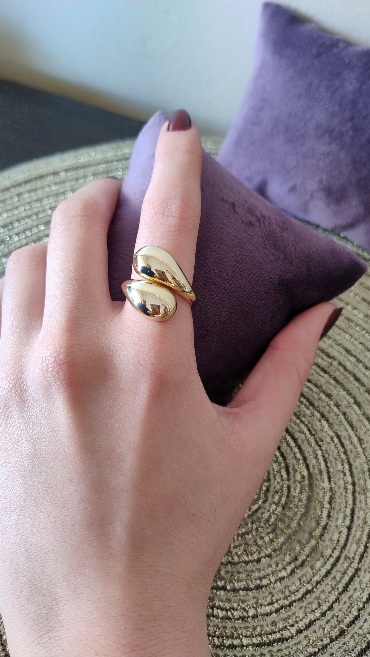 Mano con un anillo de oro de diseño estilizado, apoyada sobre una almohada morada.