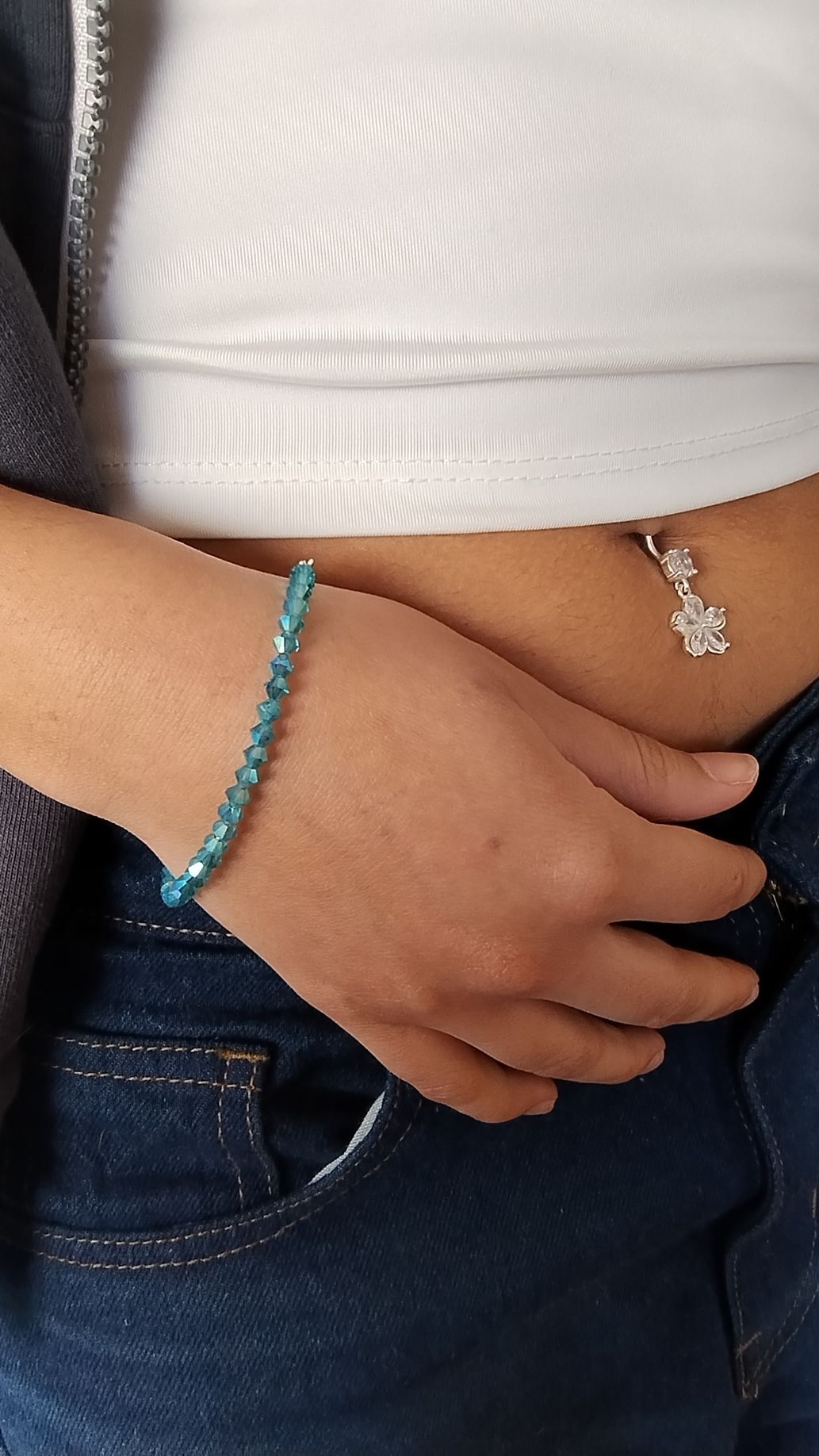 Mano que lleva una pulsera con cuentas azules. La mano descansa sobre un plato con borde dorado.