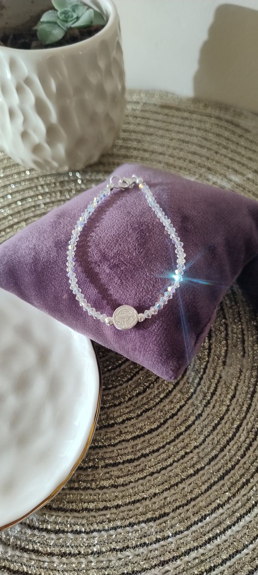 Una pulsera de cuentas de cristal sobre un cojín de terciopelo morado, con una maceta decorativa blanca al fondo.