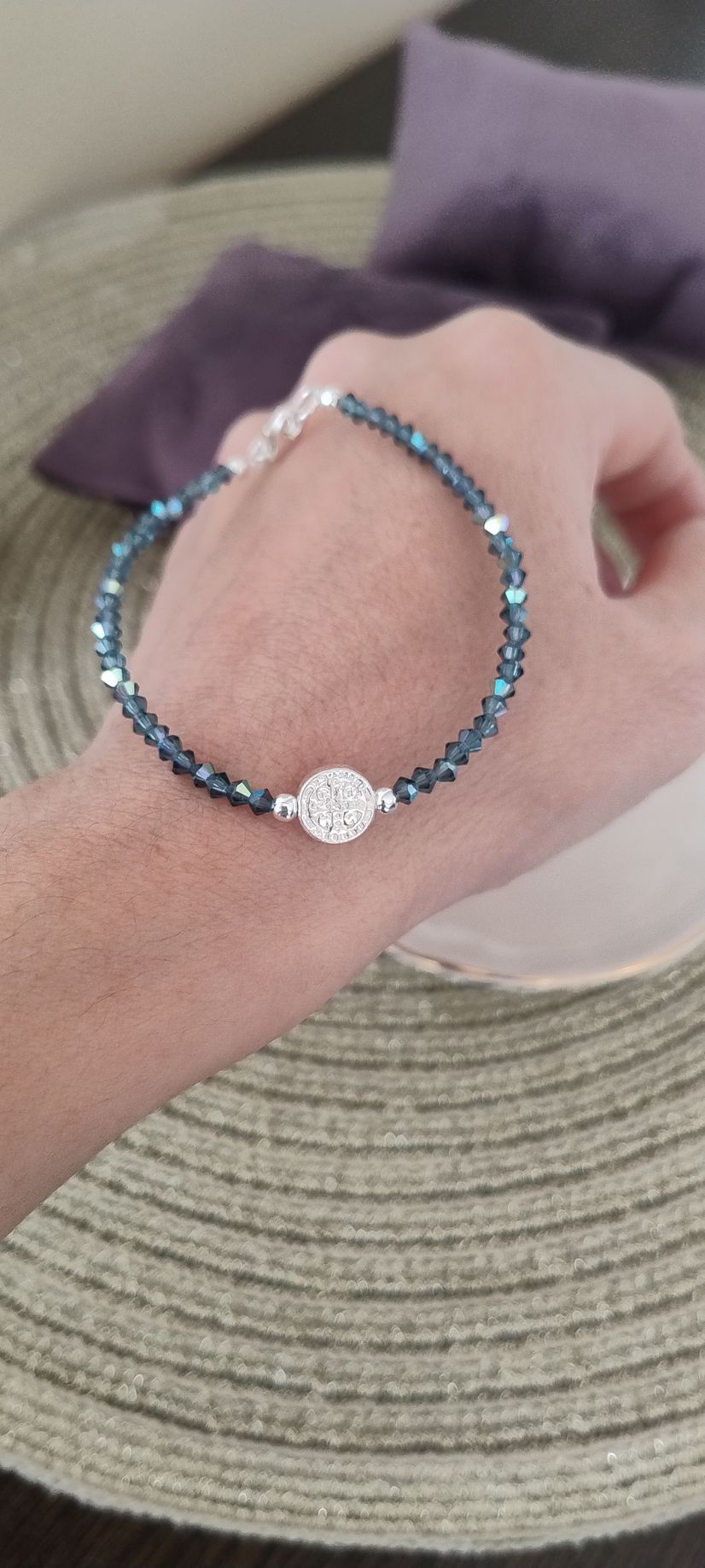 Mano que luce una pulsera con pequeñas cuentas azules y un dije floral plateado.