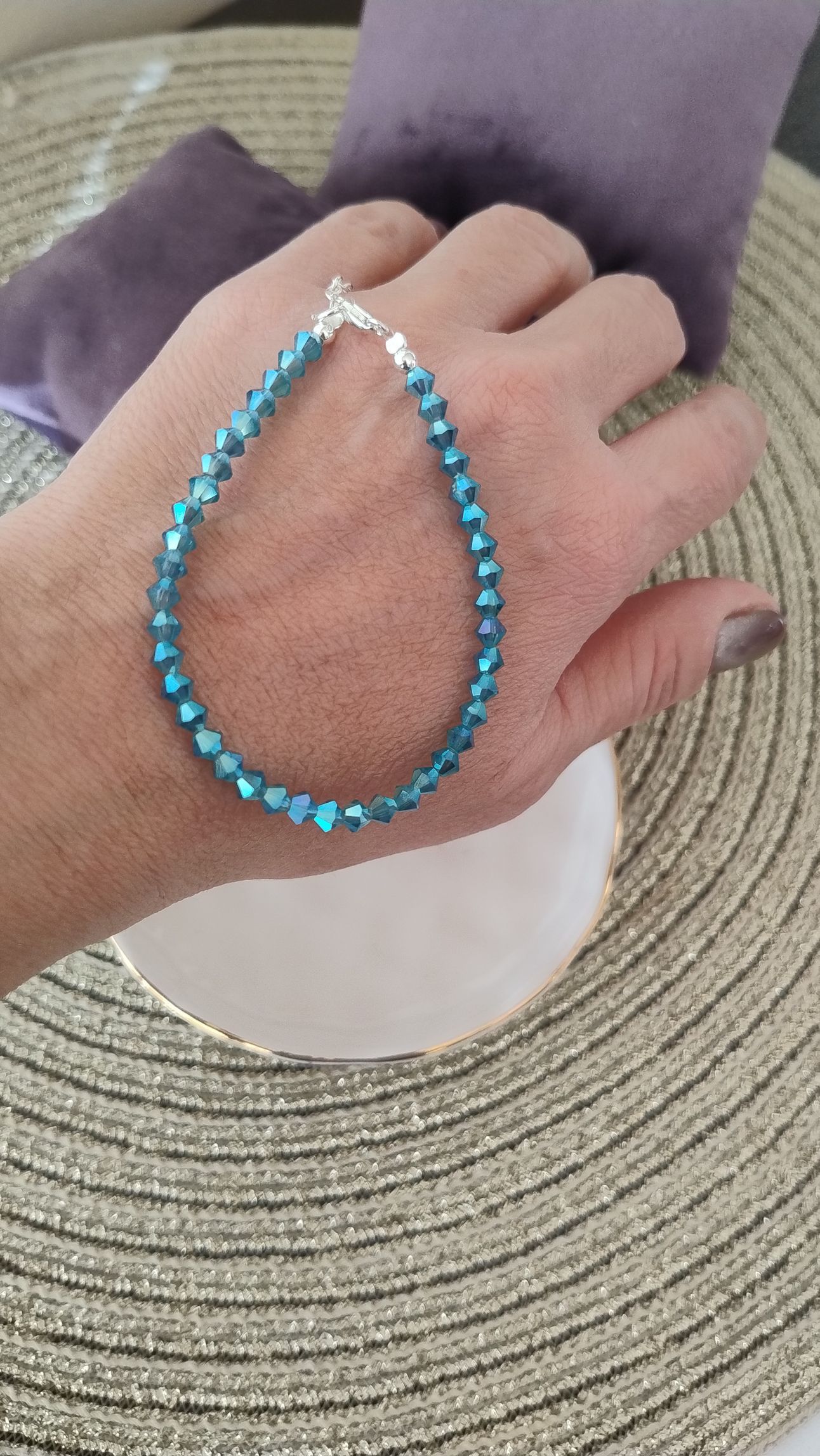 Mano que lleva una pulsera con cuentas azules. La mano descansa sobre un plato con borde dorado.