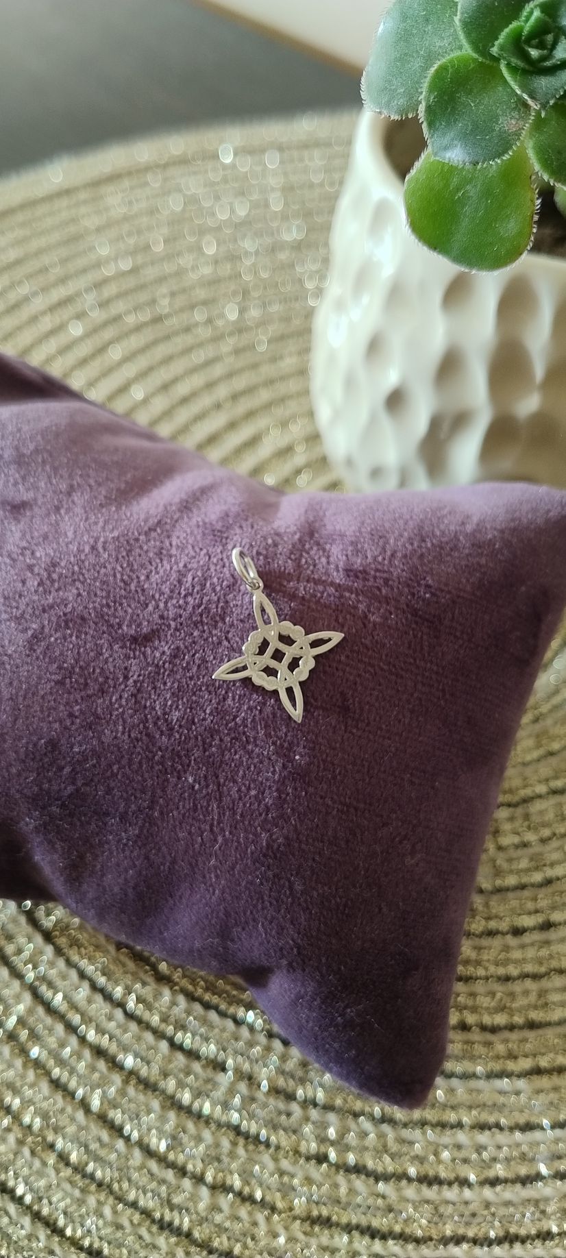 Un colgante de plata con forma de nudo de cuatro puntas descansa sobre un cojín de terciopelo morado.