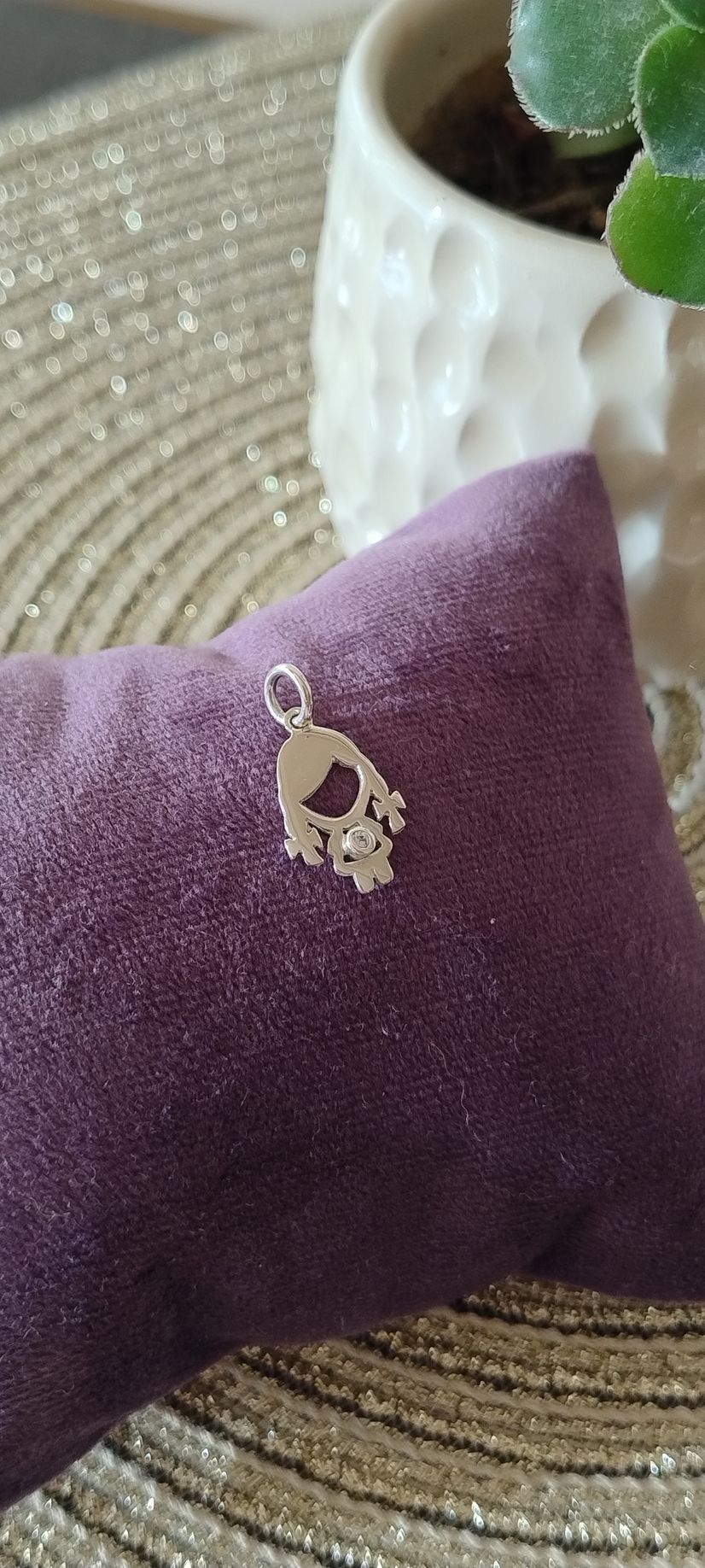 Colgante de plata con diseño de corazón y flores sobre un cojín morado.