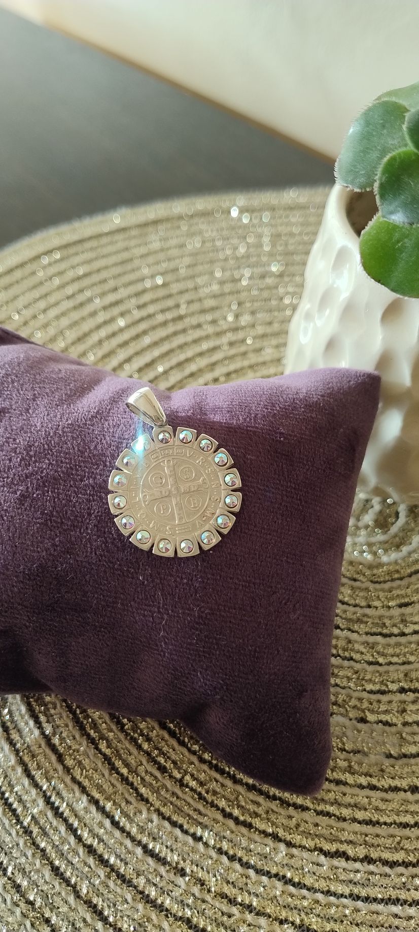 Un colgante de plata con un círculo de piedras sobre un cojín morado, junto a una maceta.