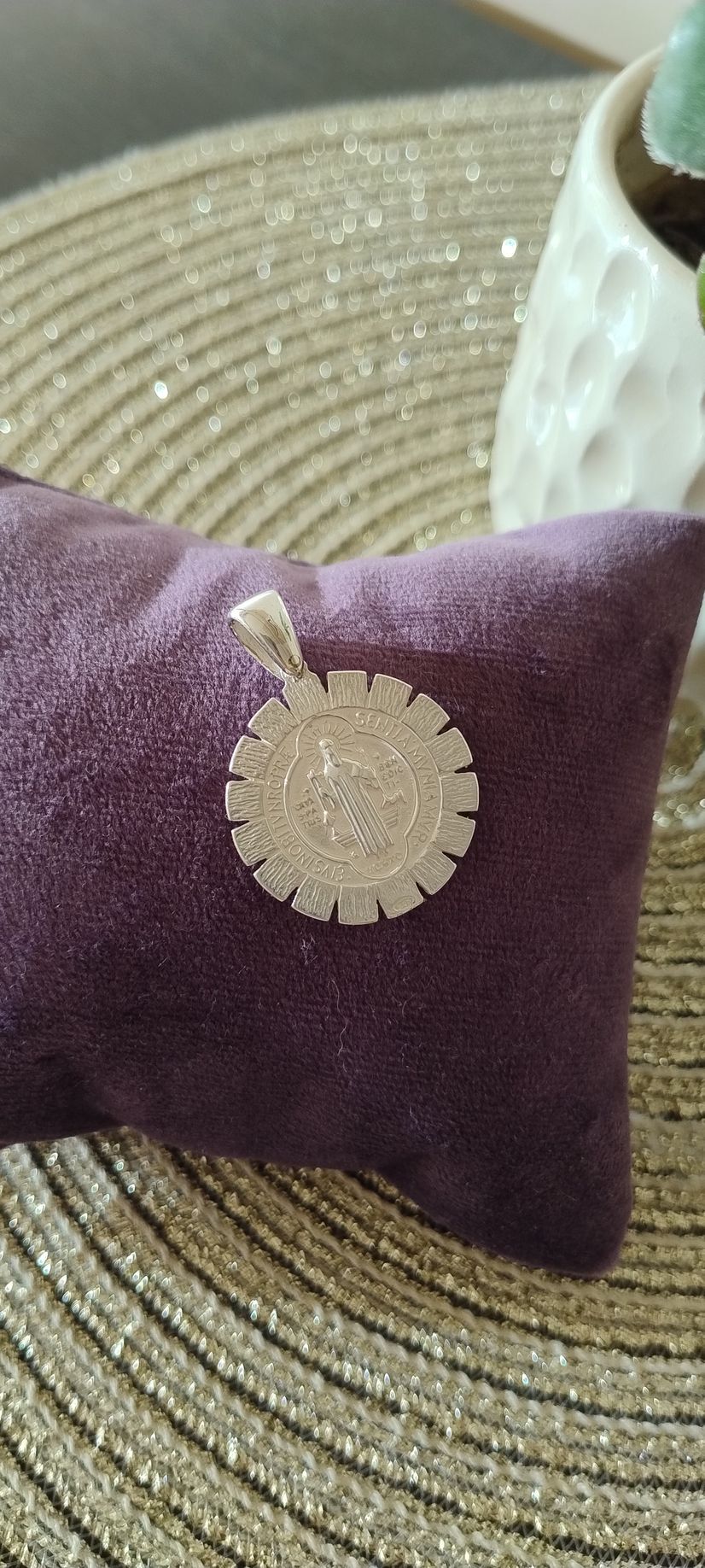 Un colgante de plata con un círculo de piedras sobre un cojín morado, junto a una maceta.