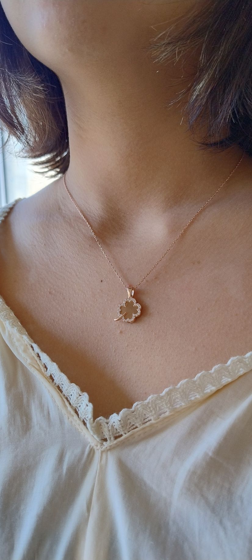 Una persona que lleva un collar de oro rosa con un colgante de trébol y una blusa color beige.