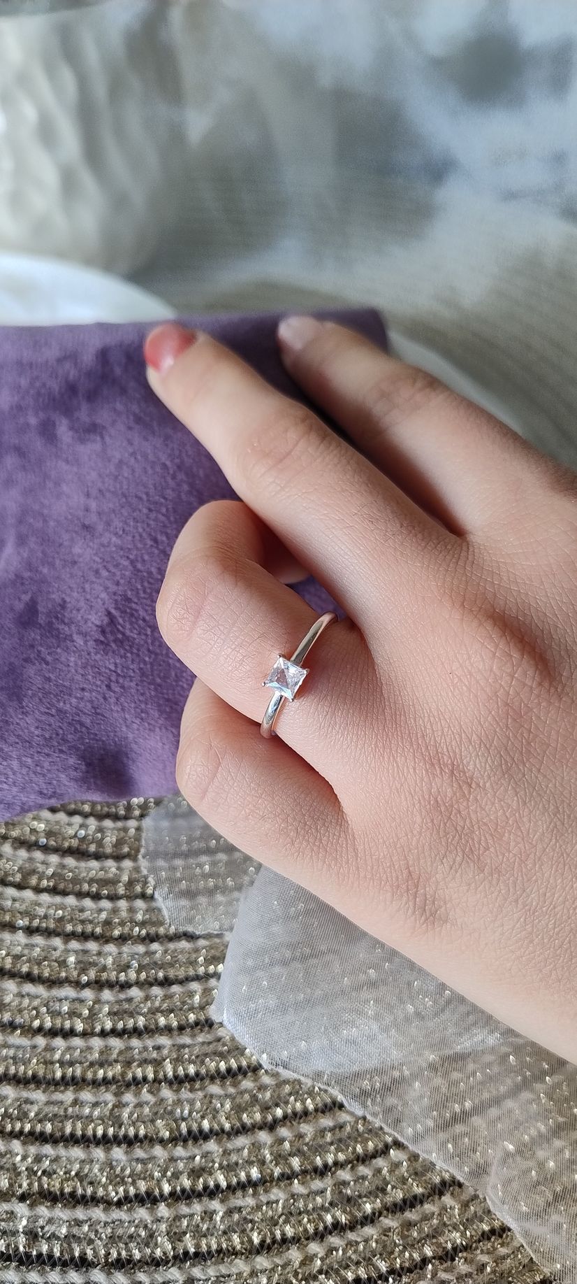 Una mano que luce un anillo con una piedra cuadrada descansa sobre una tela morada y una malla brillante.
