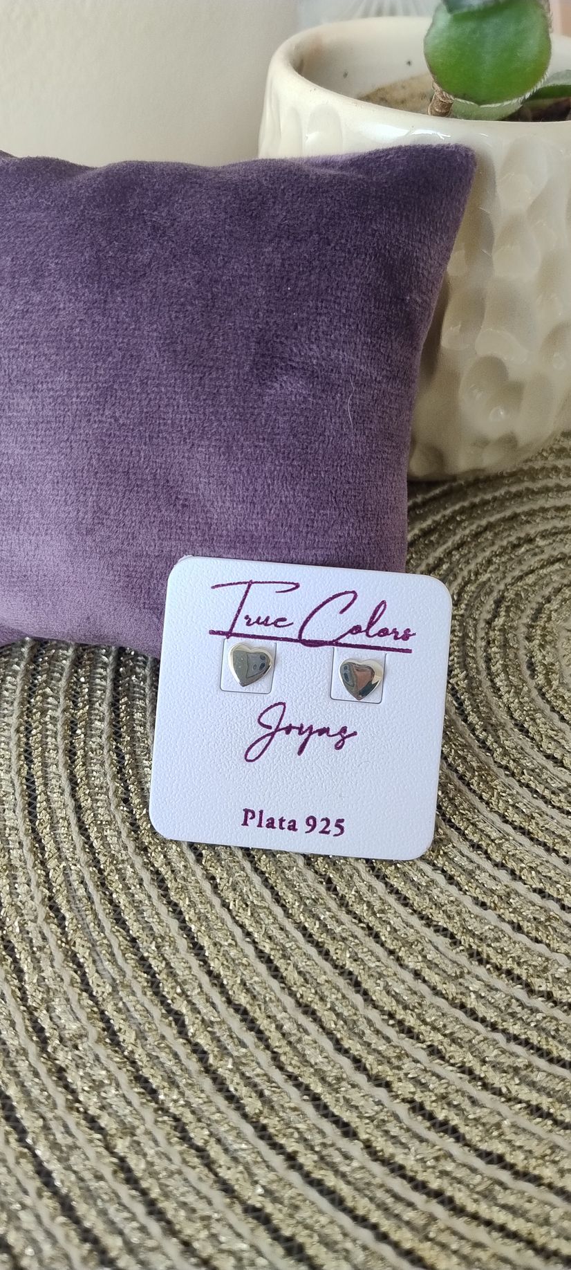 Pendientes sobre una tarjeta blanca contra un cojín morado y una superficie beige texturizada.