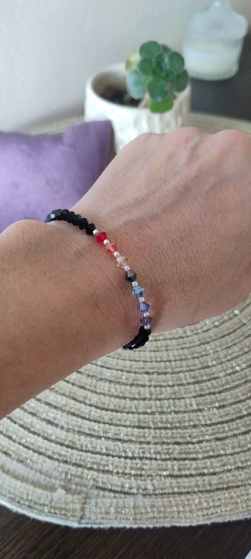 Una muñeca con una pulsera de cuentas; tiene cuentas negras, rojas, blancas, azules y moradas.