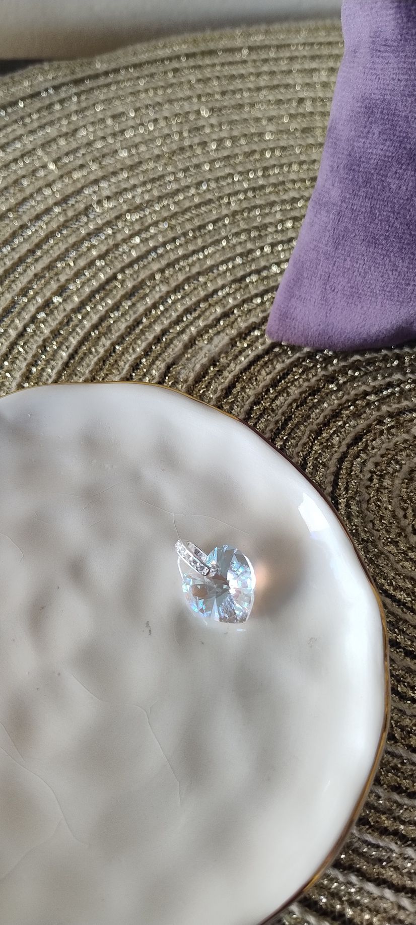 Una gema facetada de color azul claro reposa sobre una superficie blanca texturizada. Al fondo se aprecian un cojín morado