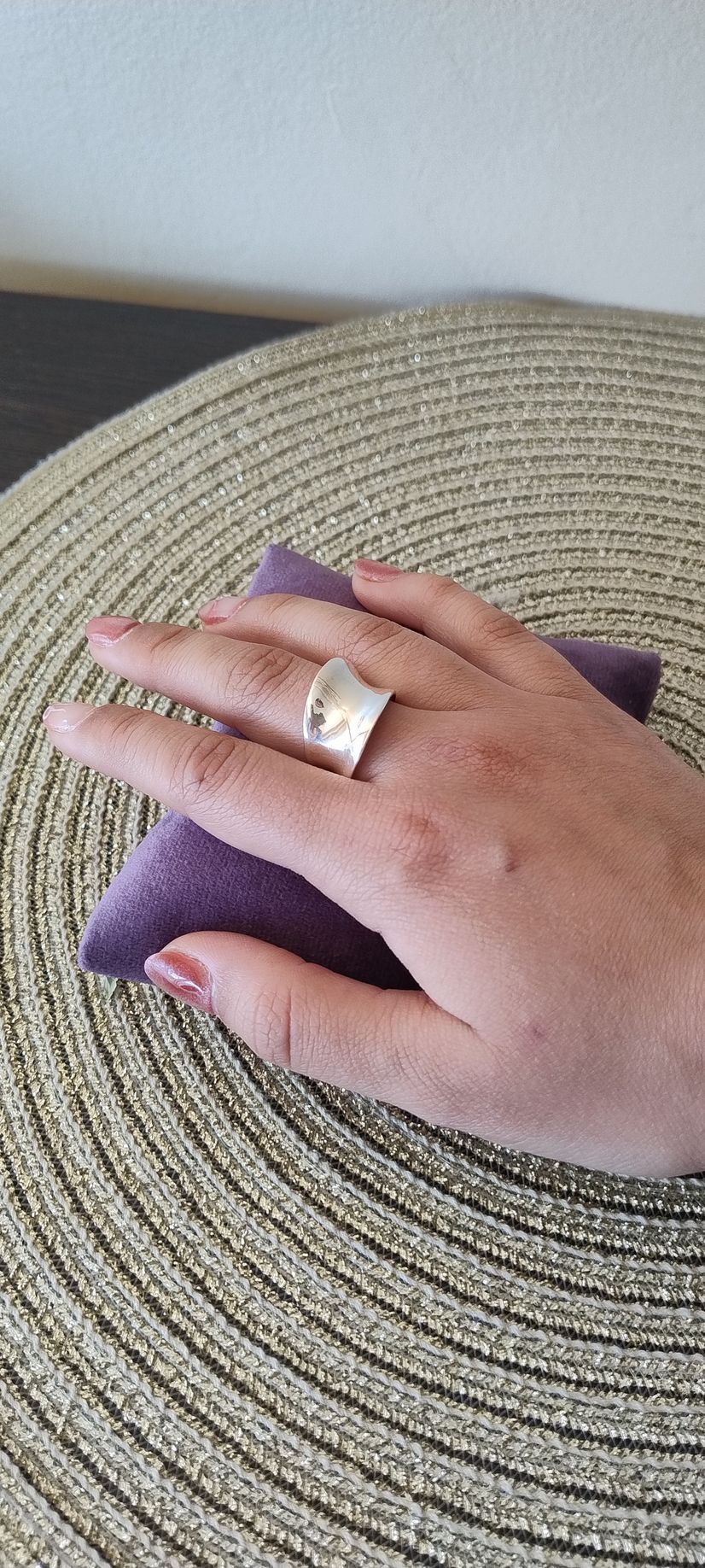 Una mano que luce un ancho anillo de plata descansa sobre un cuadrado de terciopelo púrpura,