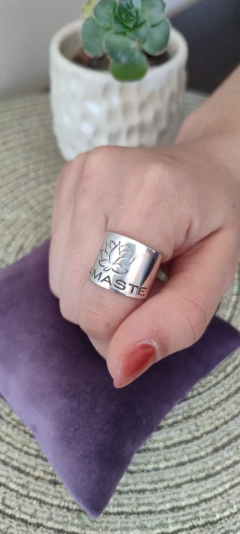 Persona que lleva un anillo ancho de plata con un diseño grabado, recostada sobre una superficie de terciopelo morado.