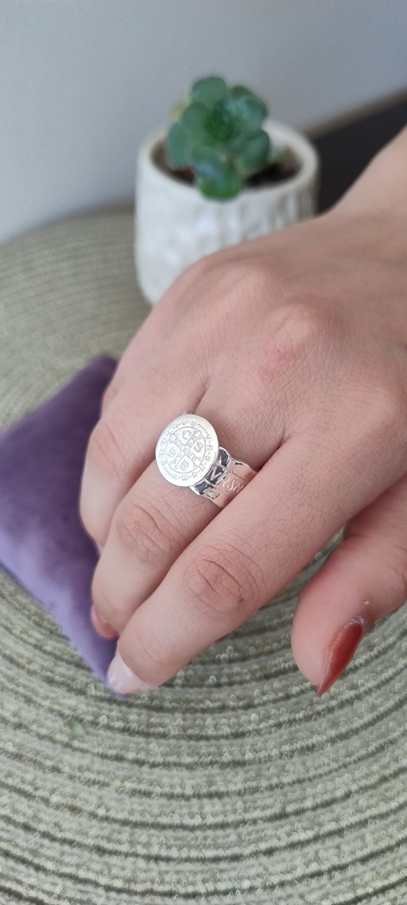Mano que lleva un anillo de plata con una gran parte superior circular, sobre una estera tejida verde.