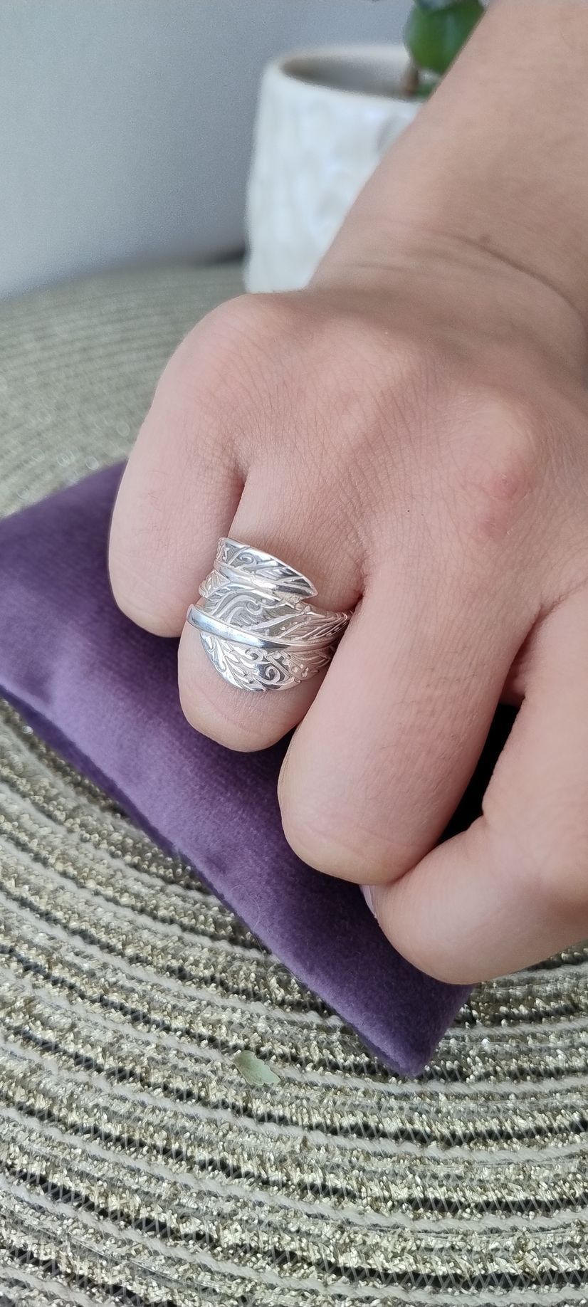 Una mano con un anillo de plata sobre una tela morada y una superficie texturizada.
