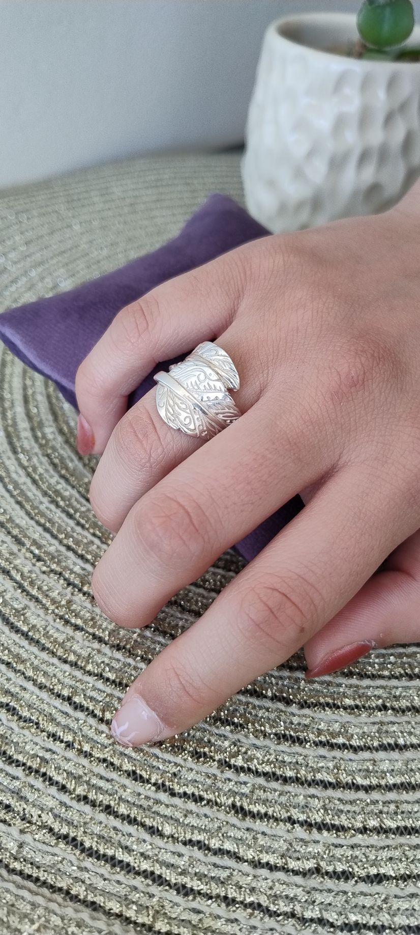 Una mano con un anillo de plata sobre una tela morada y una superficie texturizada.