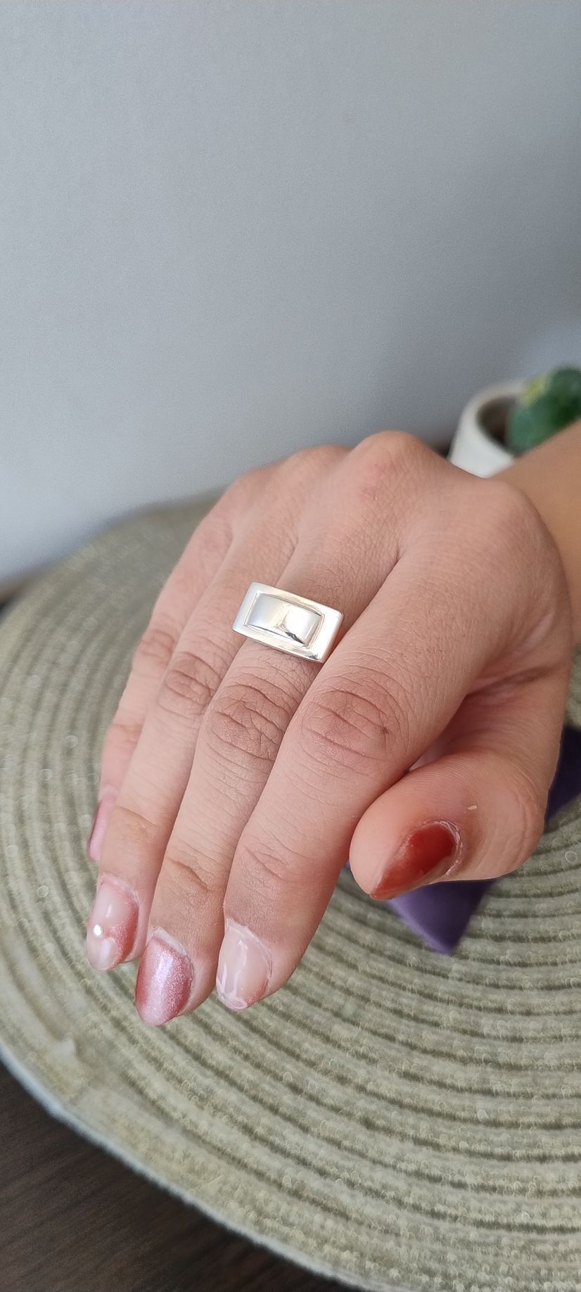 Mano luciendo un anillo rectangular de plata con un diseño.