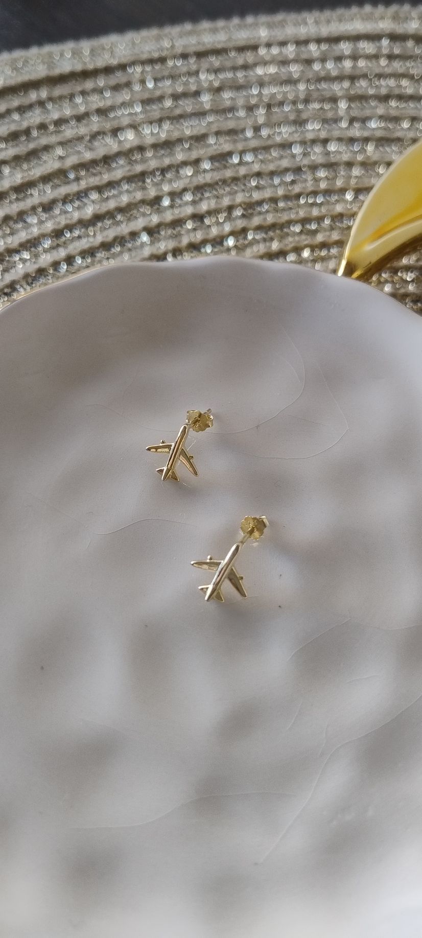 Pendientes de avión dorados sobre un plato blanco, colocado sobre una superficie texturizada.