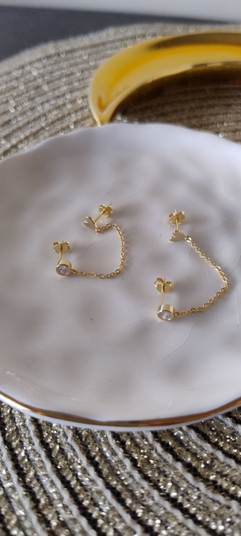 Par de pendientes de cadena dorada sobre una placa blanca con borde dorado.
