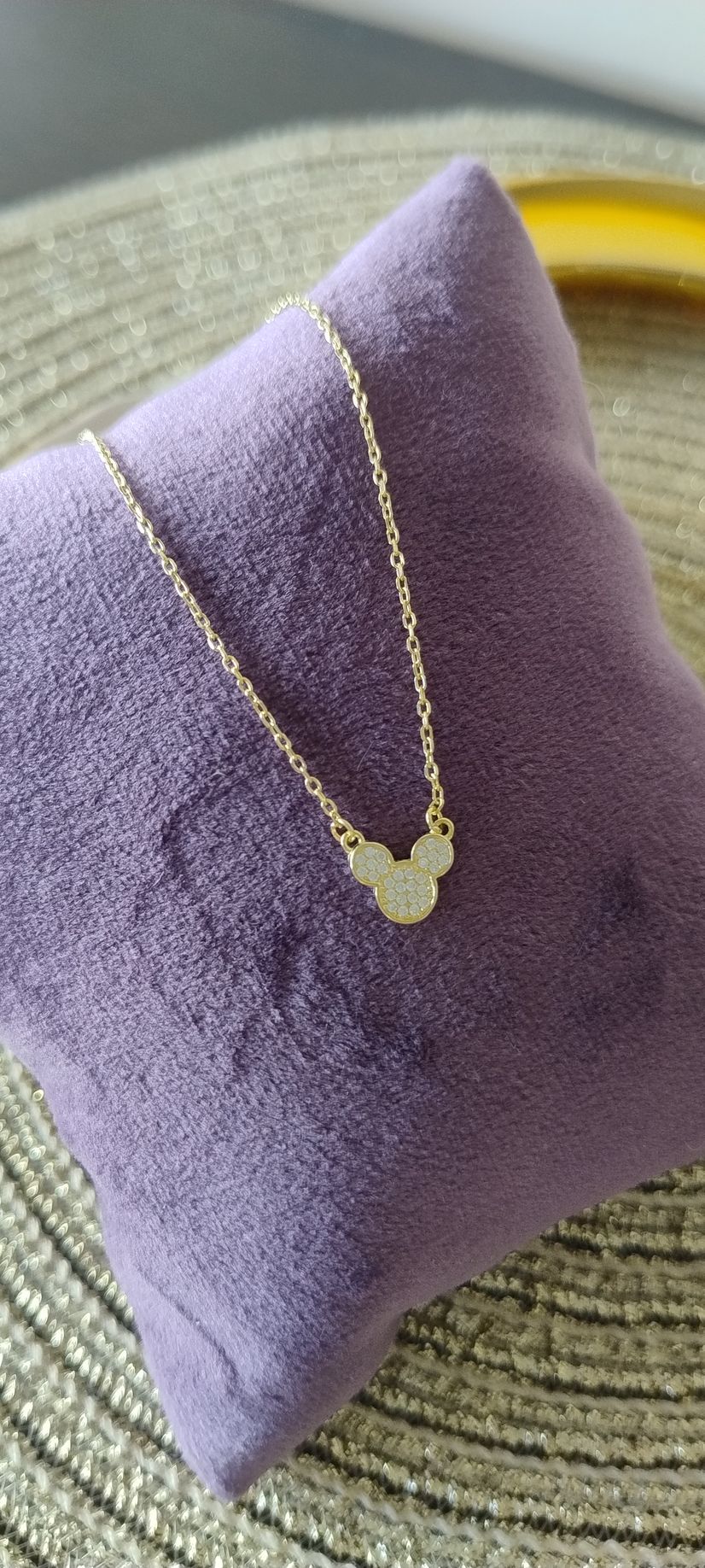 Collar de oro con colgante de Mickey Mouse sobre una almohada morada.
