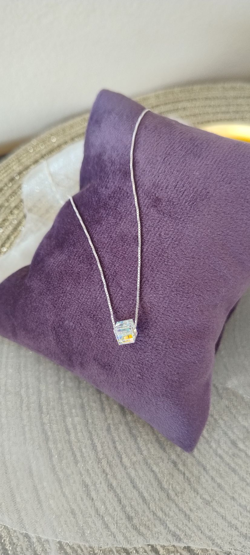 Un collar de plata con un colgante cúbico descansando sobre una almohada morada.