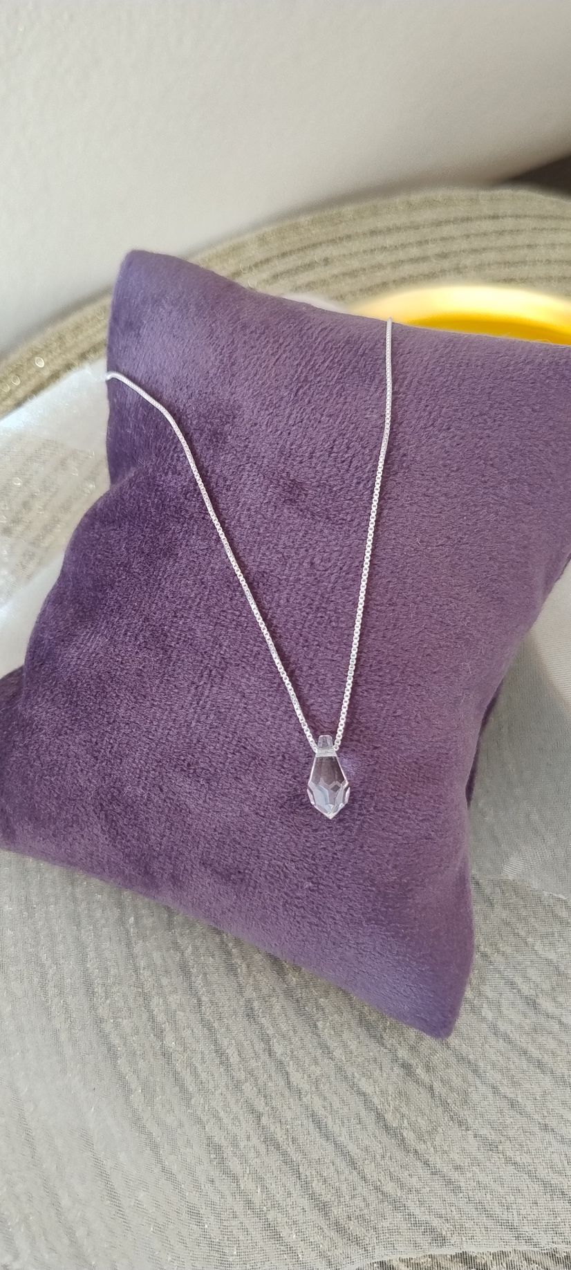 Collar de plata con colgante en forma de corazón sobre un cojín de terciopelo morado.
