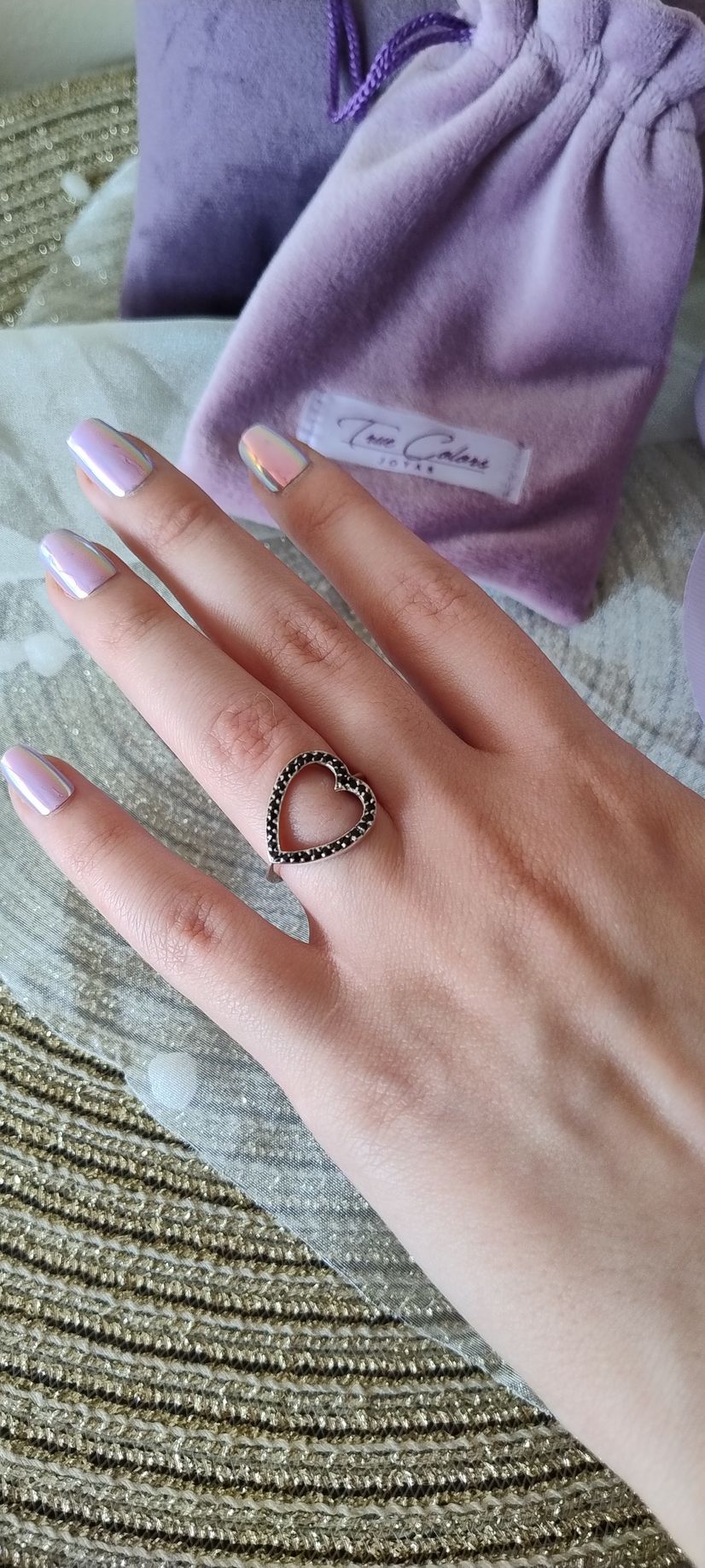Una mano con uñas largas y blancas y un anillo, descansando sobre una bolsita morada con cordón, encima de una estera tejida.