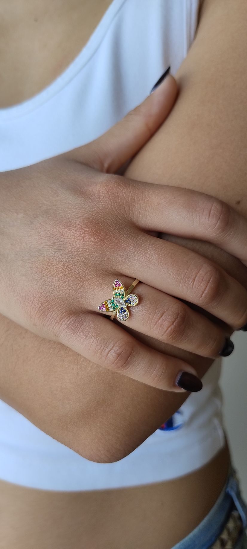 Primer plano de una mano con un anillo de piedras preciosas de colores que descansa sobre un brazo vestido de blanco.
