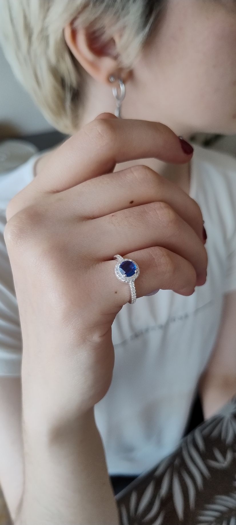 Primer plano de una mano con un anillo de plata y un colgante de piedra negra cerca del rostro, y que lleva un pendiente.
