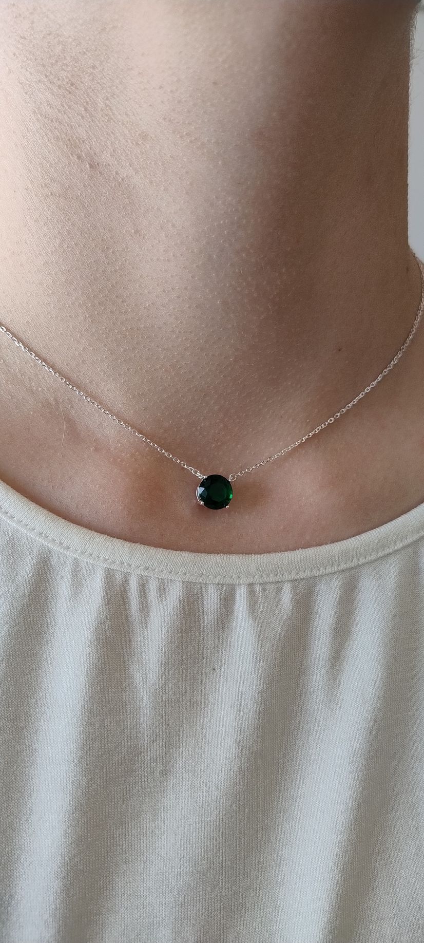 Primer plano de un collar de plata con un colgante verde sobre una base blanca.