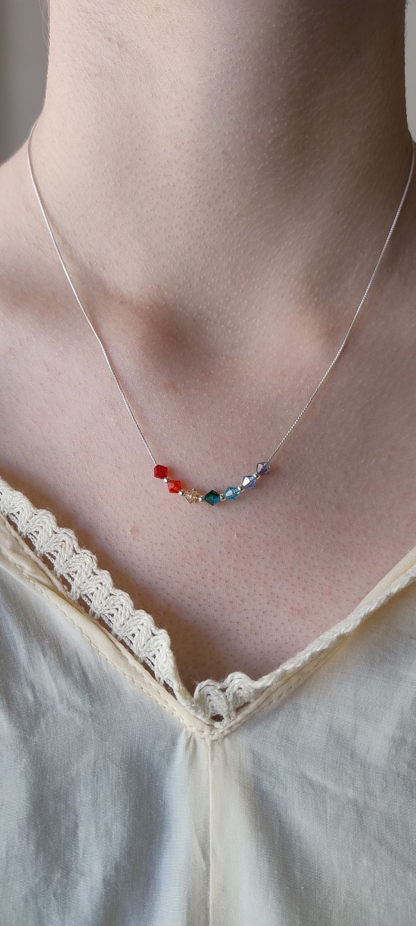 Delicado collar de plata con un pequeño colgante multicolor, llevado sobre una camisola color crema.