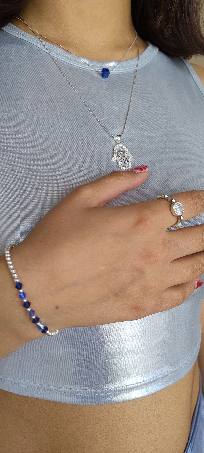 Primer plano de una persona que lleva una blusa azul claro, un collar, una pulsera y un anillo plateados en una mano