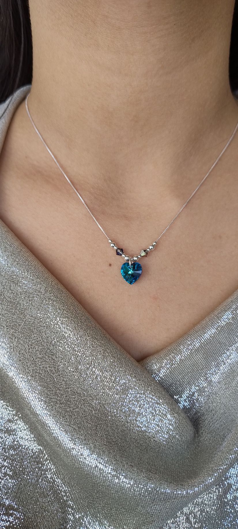 Collar de plata con un colgante azul sobre una blusa plateada brillante con escote en V.